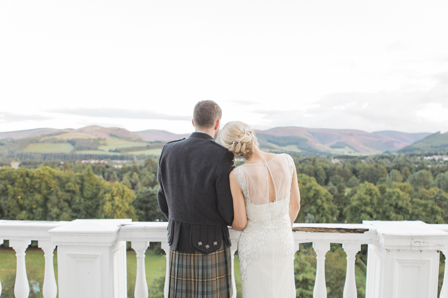 Bride rests her head on grooms shoulder as they look at the view from Peebles Hydro Hotel balcony